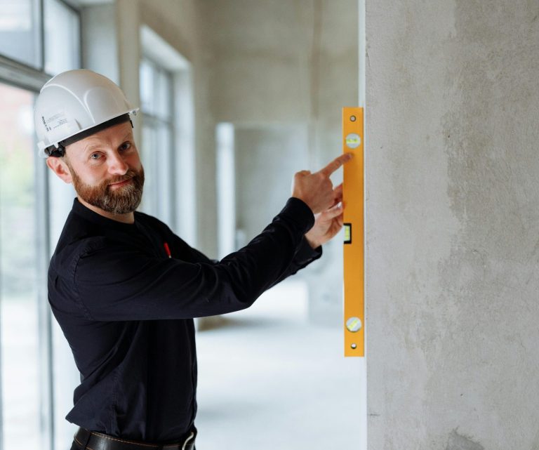 Baustelle Handwerksservice Mann mit Helm zeigt auf ein Wasserwaage an einer Wand in einem Bauprojekt.